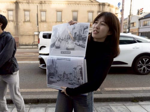 まちあるきのリーダーが、過去の周辺写真を見せながら昔と今との繋がりを伝えています