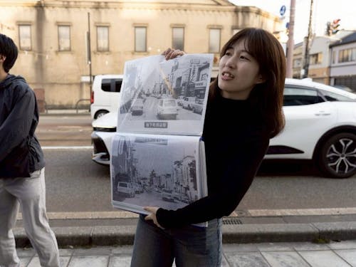 まちあるきのリーダーが、過去の周辺写真を見せながら昔と今との繋がりを伝えています