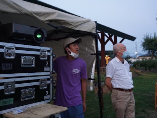 広い公園で屋外上映会を開催中、プロの顔を覗かせる安倍さん(写真左)