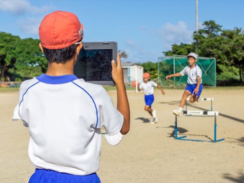 タブレットで同級生のハードル走を撮影する児童