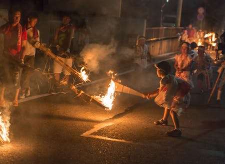 行列に地元の子供たちが割って入り、松明の火が燃え過ぎないようバンバラ竹でに力いっぱいたたく！