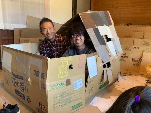 子どもたちのつくったダンボールハウスの中の山本さんと谷村さん