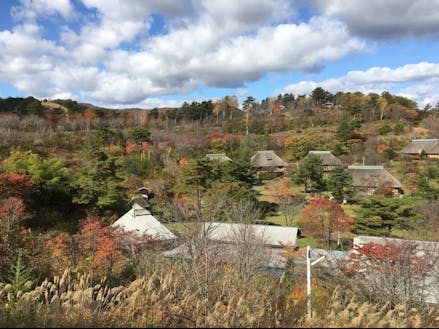 秋の始まりの「タプコプ創遊村」。丘の上から古民家の茅葺屋根が５棟見える。