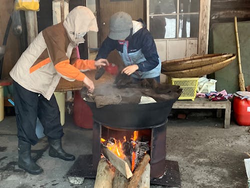 味噌つきの豆を大きな鉄鍋で薪をくべて煮る