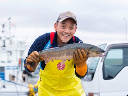 チャーミングな笑顔で秋鮭を持つ漁師さん